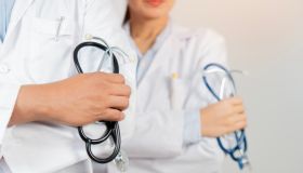 Cropped image of two determined physicians wearing white medical gowns standing and holding a stethoscope