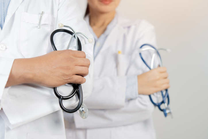 Cropped image of two determined physicians wearing white medical gowns standing and holding a stethoscope