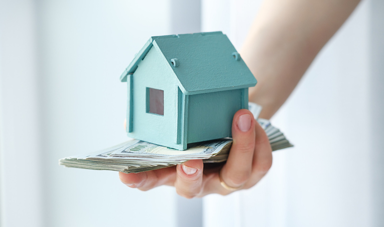 A person is holding a house model and a stack of bills