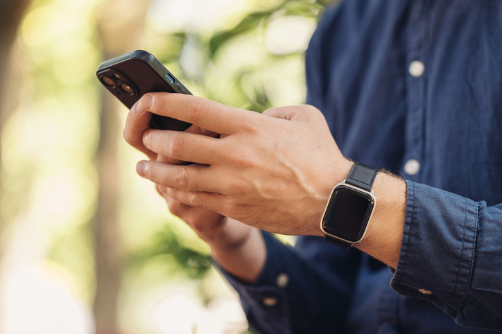 A young man is using his smartphone while enjoying the outdoors, also wearing a smartwatch