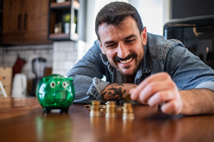 Happy man stacking coins at home with piggy bank
