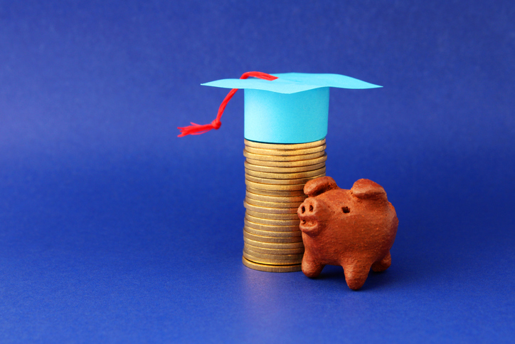 Graduate cap next to a piggy bank and gold coins, cost of education