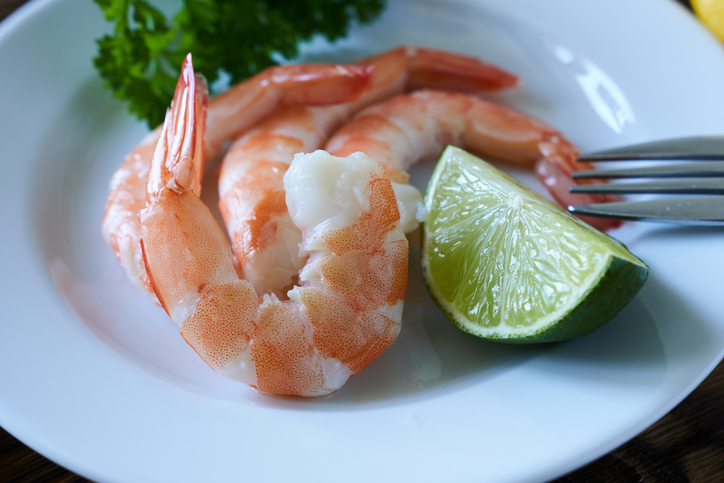 Boiled shrimp with lime and parsley on a white plate.