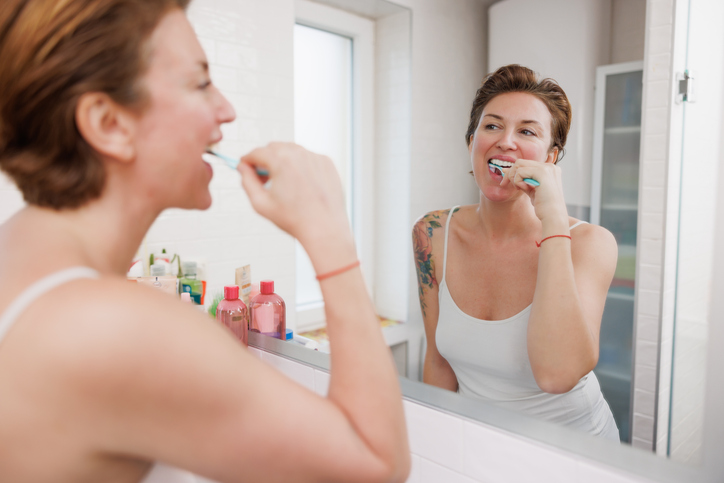 Beautiful middle-aged woman brushing her teeth in front of the bathroom mirror, daily healthcare