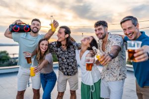 Happy friends enjoying rooftop party with music and drinks