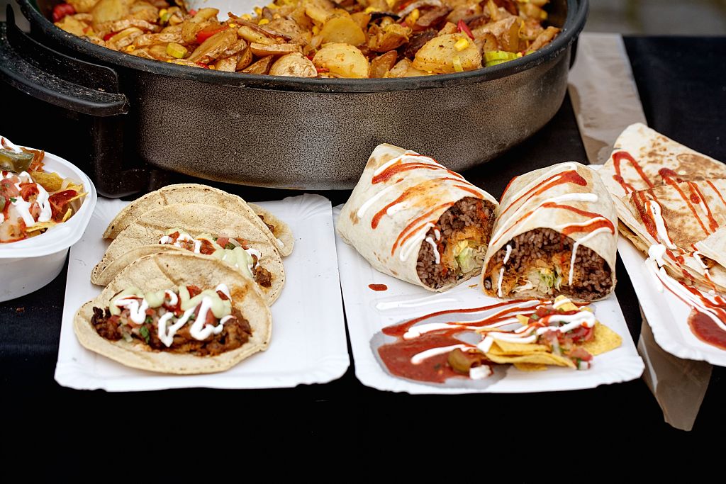 Delicious Mexican Street Food Display with Beef Tacos Burritos Nachos And Frying Pan with Potato Mix. Authentic Cuisine Served on Disposable Plates with Sauce