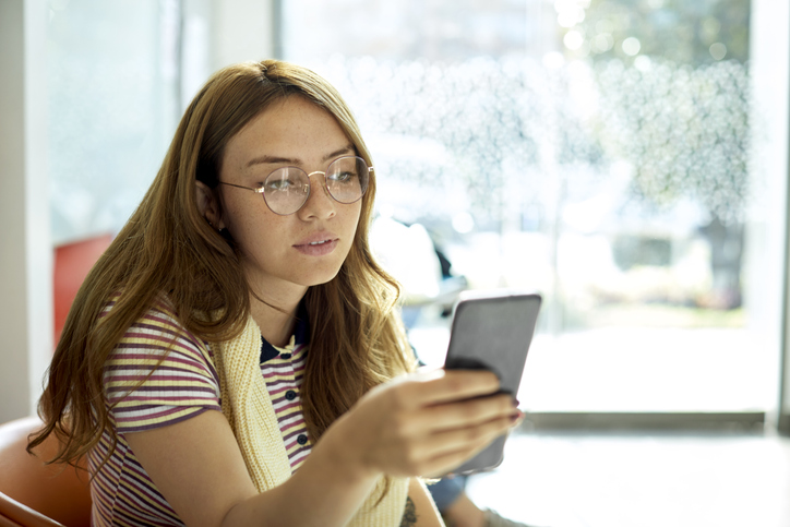 Young female student using phone in cafeteria