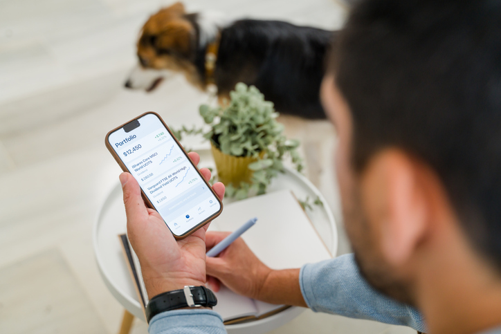 Man investing in stocks using smartphone and writing notes