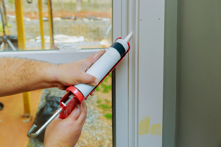 Hand applying sealant to window frame during home improvement project in bright, natural light