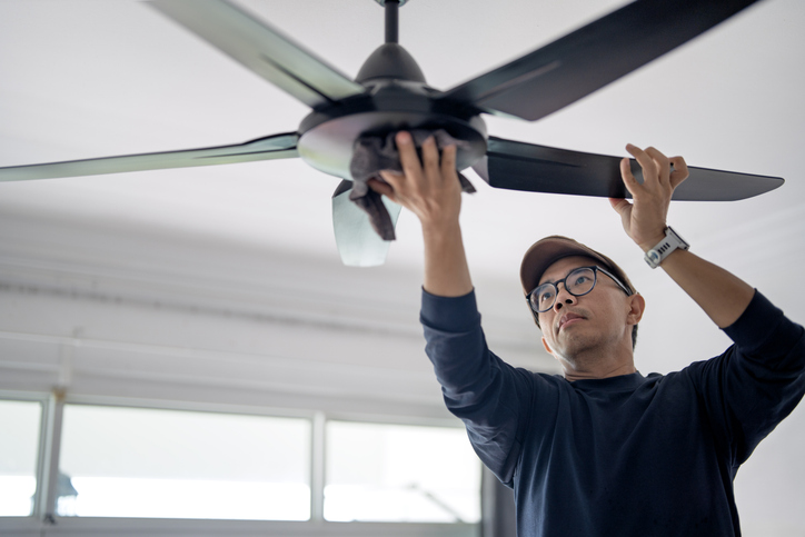 Man cleaning ceiling fan at home
