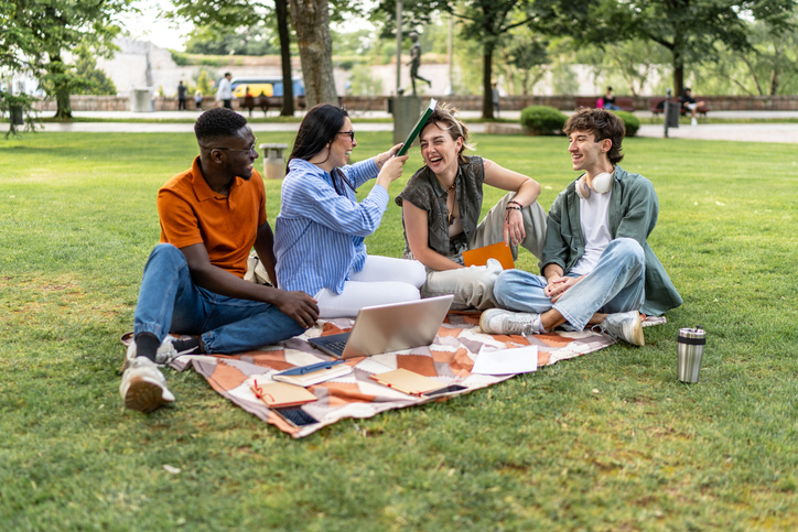 Diverse students studying and having fun outdoors on green grass