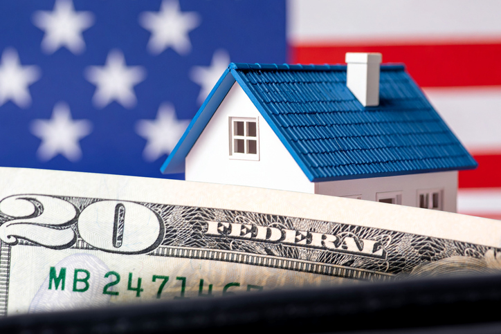 Dollar bills, a house, and an American flag in the background