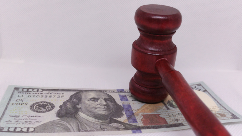 Court gavel resting on hundred dollar bill depicts legal fees or financial crimes concept