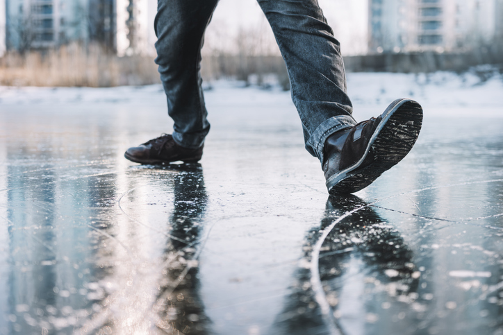 Boots standing on icy ground, illustrating the danger of slipping on a frozen, slippery winter surface. man walks cautiously along an icy street on a winter day for fear of slipping and falling.
