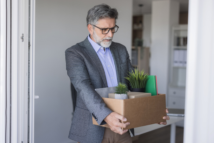 Sad businessman leaving office after losing his job, carrying cardboard box