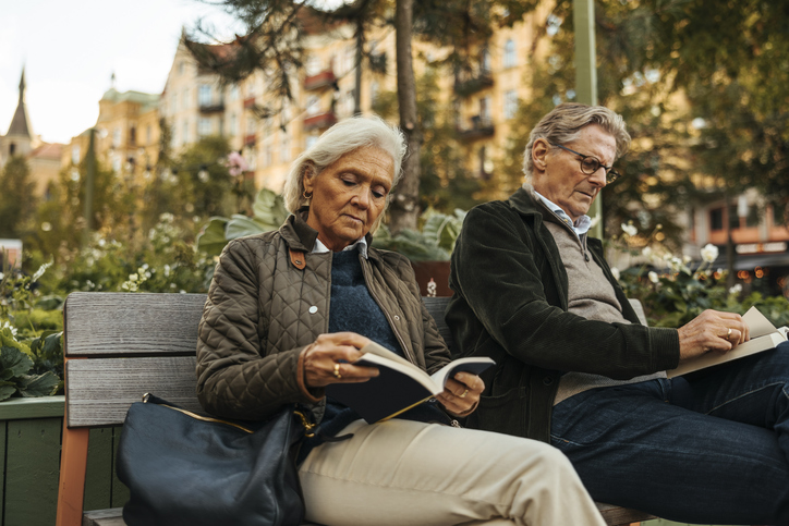 Senior woman reading book with man while sitting on bench