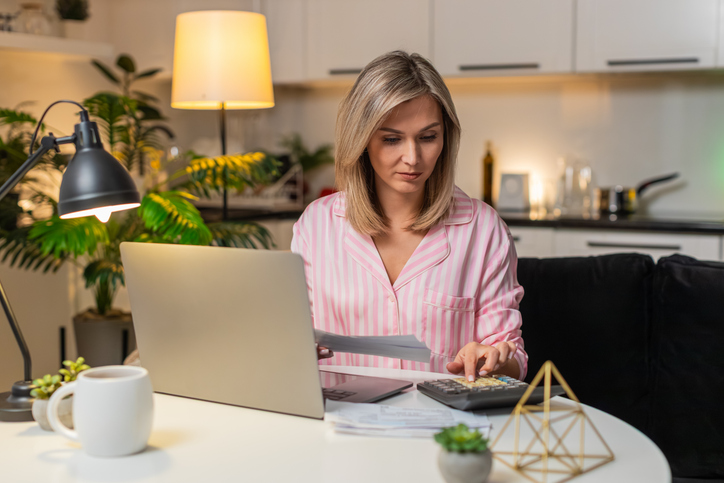 Adult woman with laptop and calculator tracks budget marks bills paid notes savings manages expenses