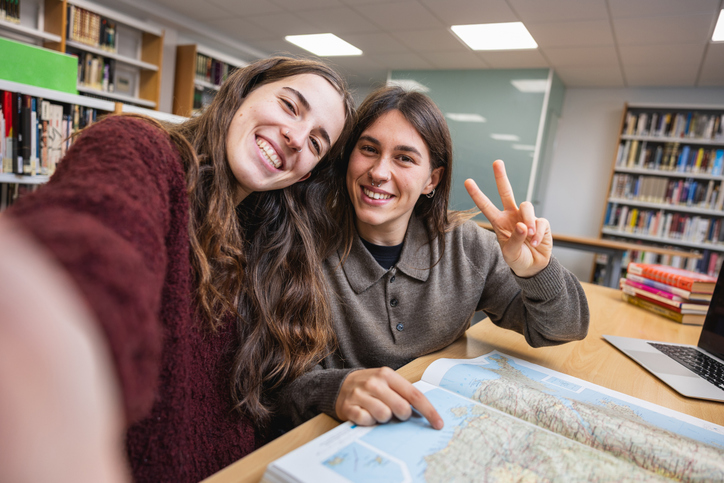 Friends snapping a selfie while mapping out their next trip in the library.