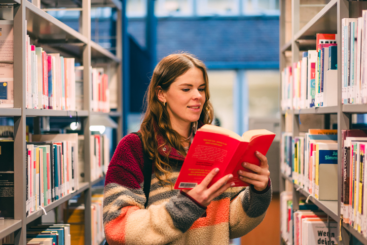 Young Woman Choosing Book In Modern Library