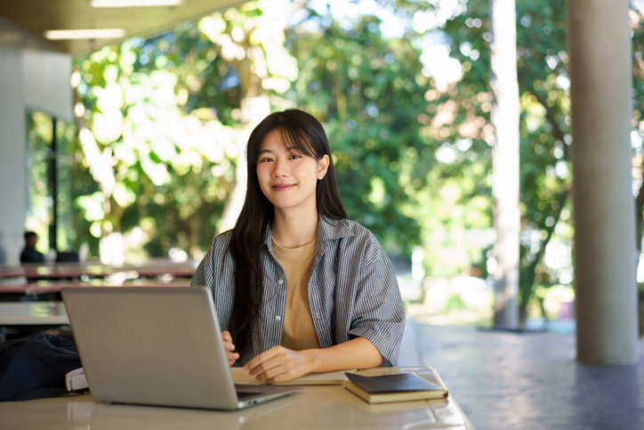 Education, university and woman in campus, research and books for school project or exam. Laptop, notebook and internet, college student studying with technology and e learning on campus