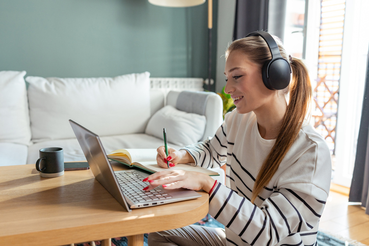Young woman with headphones, studying with a laptop, smiling and focused in a cozy living room