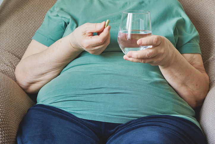 Senior woman taking medication with glass of water for health and wellness