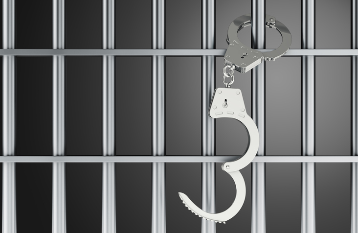 Handcuffs hanging on prison bars, arrest and incarceration concept. 3D rendering