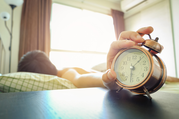 Hand reaching out to turn off or snooze a vintage alarm clock in the bedroom at morning, waking up for a new day and daily routine .health and relaxation concepts.