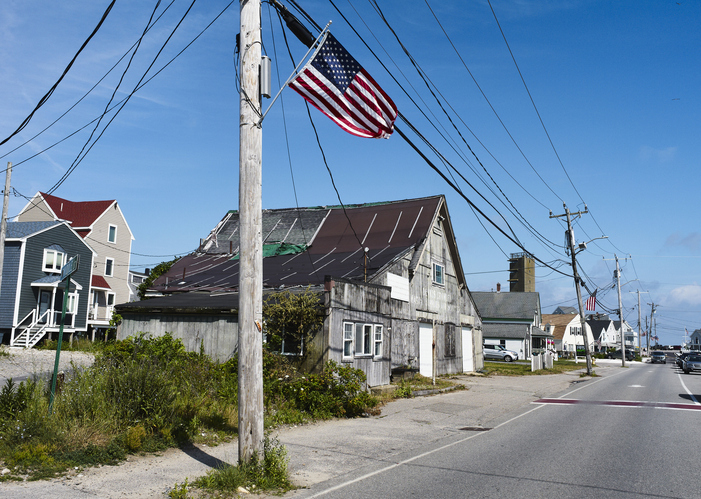 Weathered building on a street with an American flag under a clear blue sky. Marshfield, USA