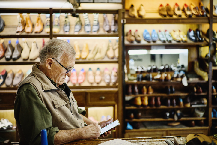 Medium shot senior shoe shop owner looking at smart phone in store