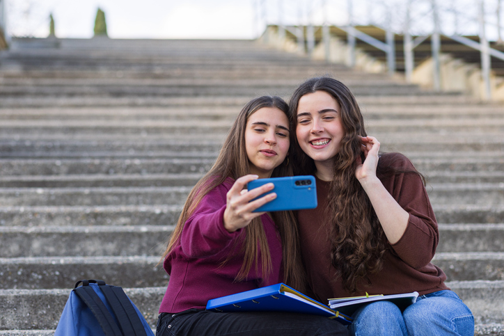 Two happy teen girls taking selfie on campus stairs