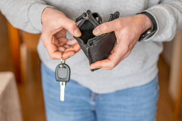 Person's hands holding an empty black leather wallet and a car key, symbolizing the financial struggle and rising costs of fuel amidst inflation and an economic crisis