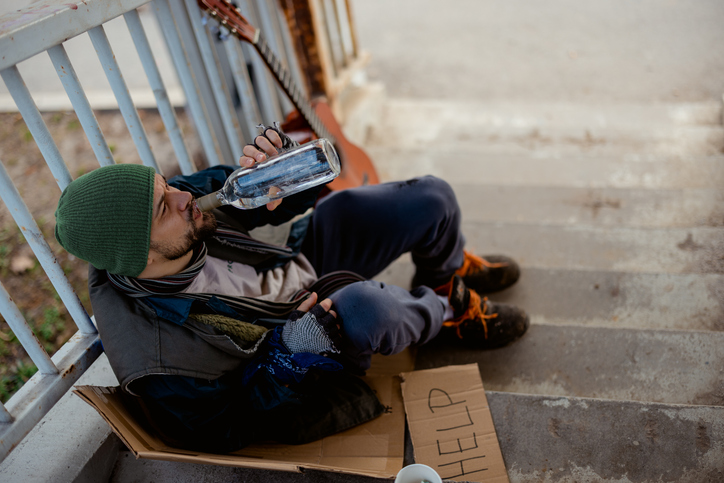 Homeless Man Resting on City Underpass Steps With Bottle