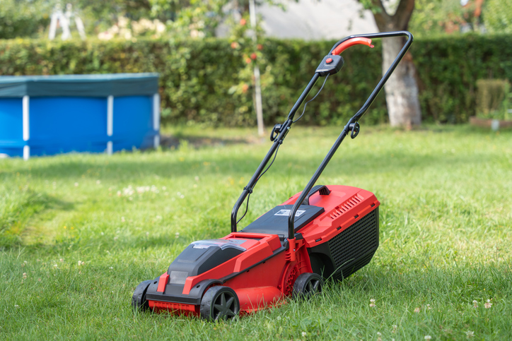A red lawn mower stands on green grass in a backyard.