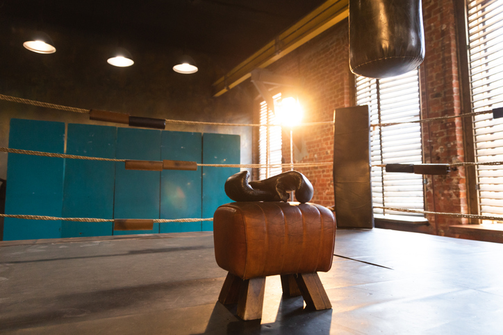 Boxing gloves lying down on boxing ring in empty gym. Equipment for fight training competition black protective boxing gloves ready for fighter winner on ring. Strength fit body workout training.