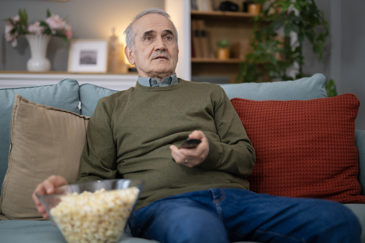 Senior man watching television consuming popcorn at home