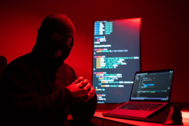 Hacker in balaclava with an obscured face is stealing data, representing cybercrime, hacking, dark web activity, and online security threats. Cyber Security concept.