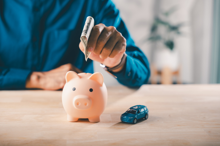 man puts money to save in piggy bank for car insurance fuel price cost auto finance gas tax saving, person inserts dollar near blue vehicle model for future travel budget expenses