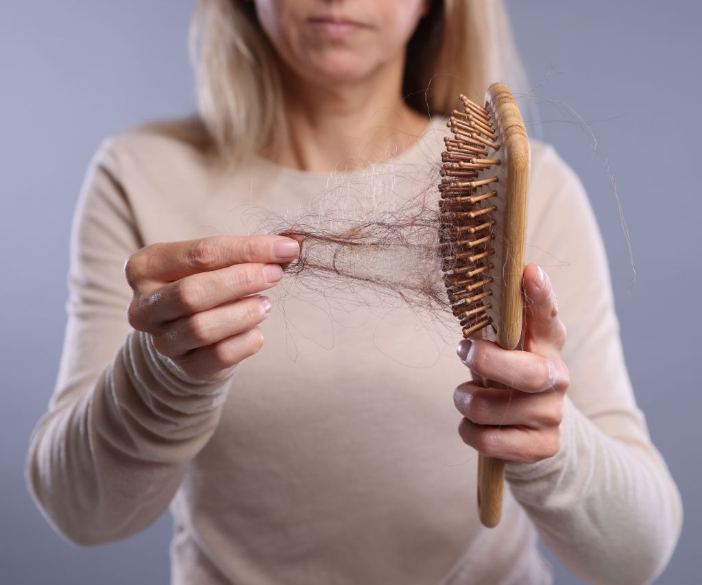 Alopecia problem. Woman taking her lost hair from brush on grey background, closeup