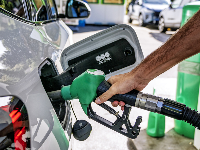 A man's hand holding a fuel hose, refueling an unleaded gasoline vehicle using a self-service pump and hose.