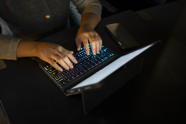 Close up shot: A female hand typing on a keyboard using a laptop in the dark. Working overtime until late, conducting online banking transactions, and integrating technology into daily life
