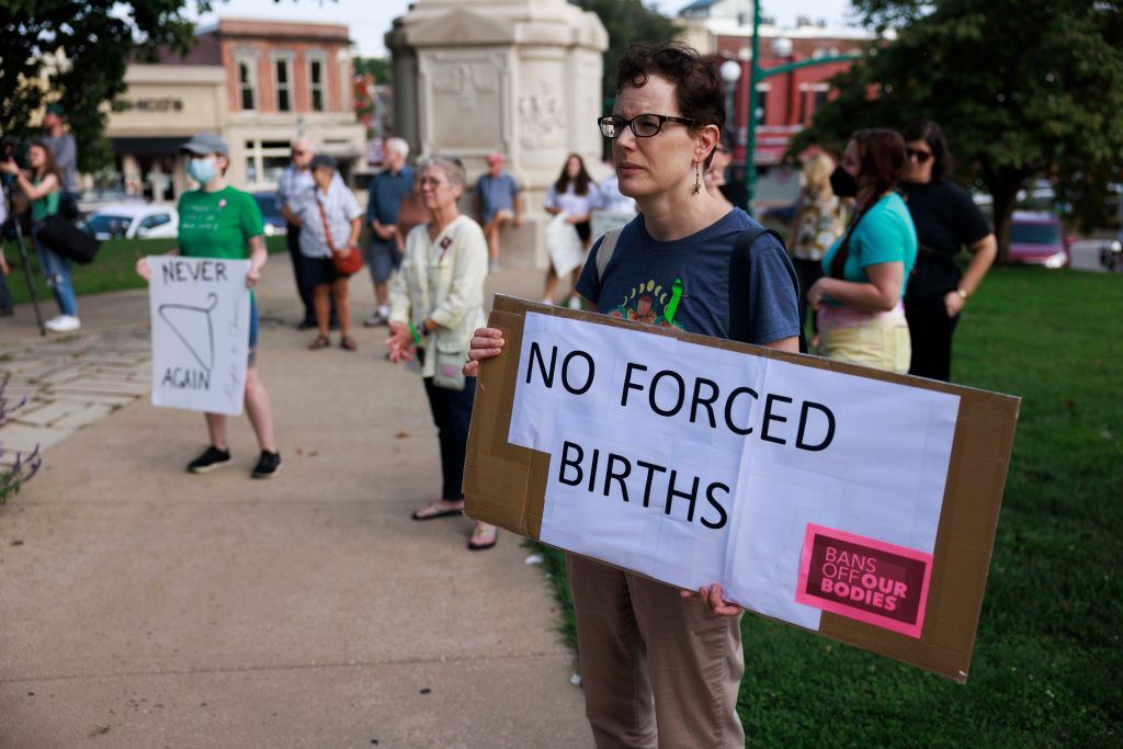 A woman holds a placard saying, No Forced Births, as