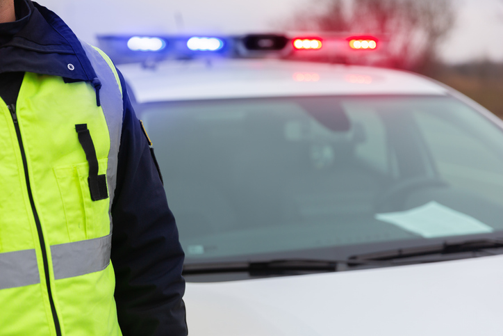 Police officer standing by patrol car with flashing lights