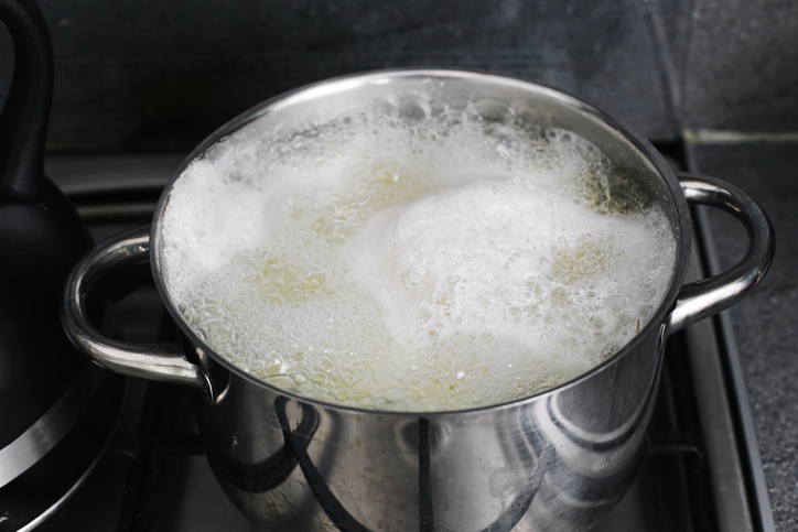 Boiling pot with water foam overflowing on stove. Kitchen problem of boiling over and cleaning after cooking.