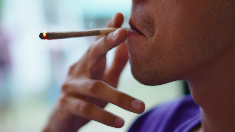 Person exhaling smoke from a lit marijuana joint, consuming cannabis