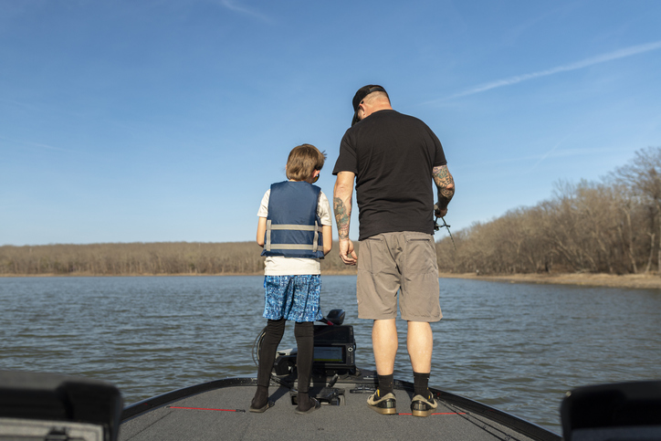 Back view of a father and son standing on boat looking at fish finder