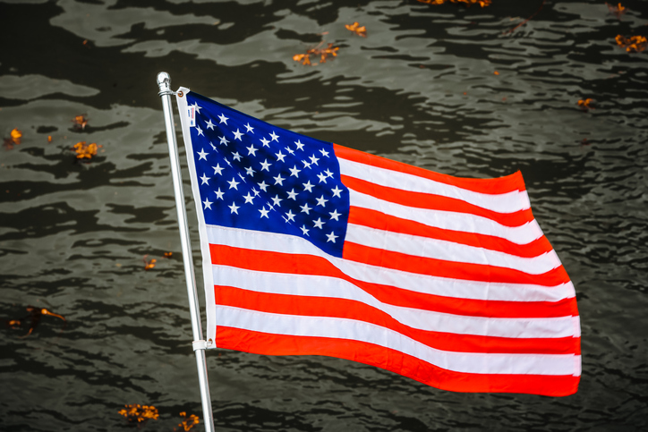 United States flag blowing in the wind on a metal pole above the rippled surface of the Gastineau Channel in Alaska