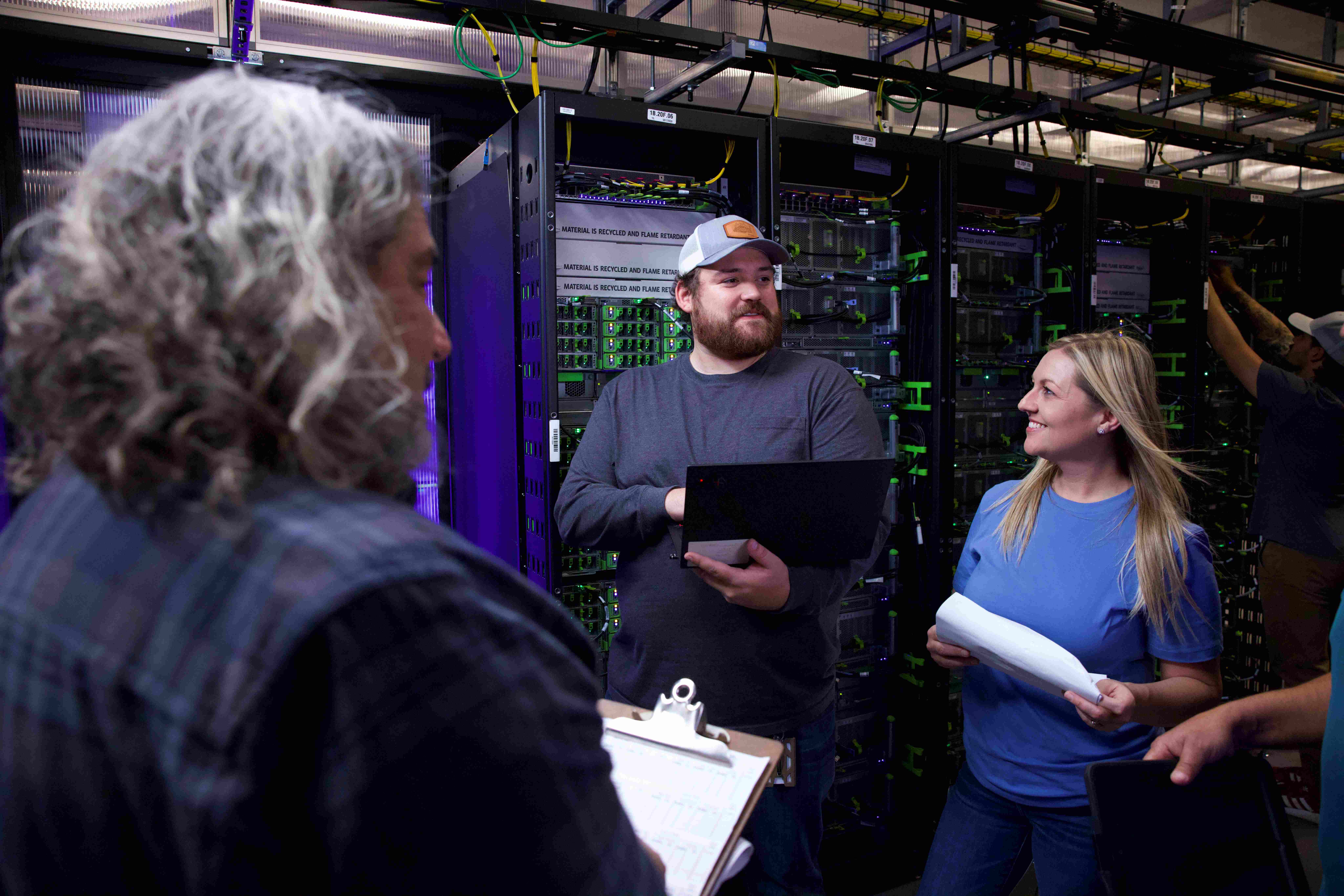 Three people in a data center, one holding a laptop and discussing with the others.