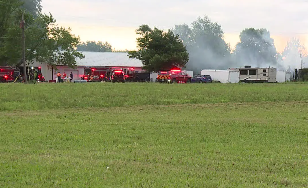 A grassy field with several red fire trucks and a recreational vehicle parked on the grass.