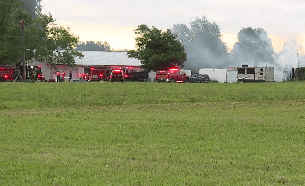 A grassy field with several red fire trucks and a recreational vehicle parked on the grass.